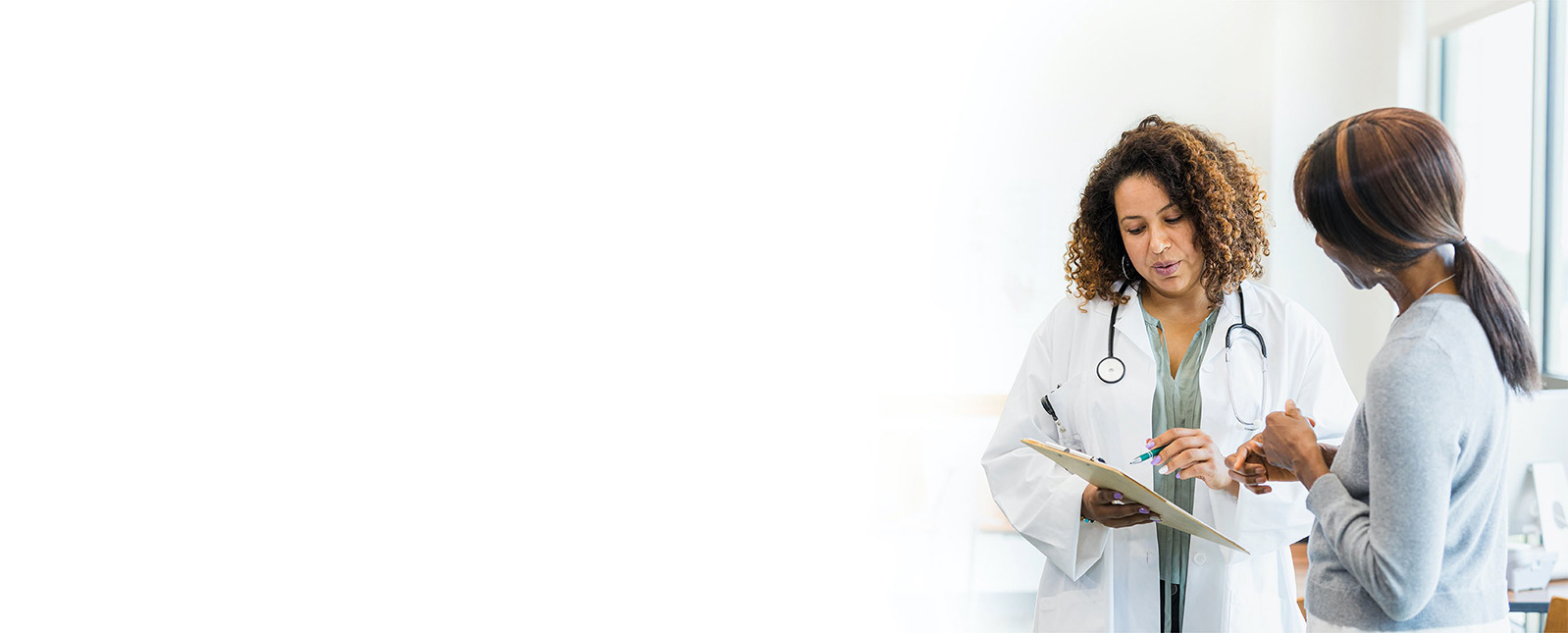 A healthcare provider reviewing information on a clipboard with a female patient.