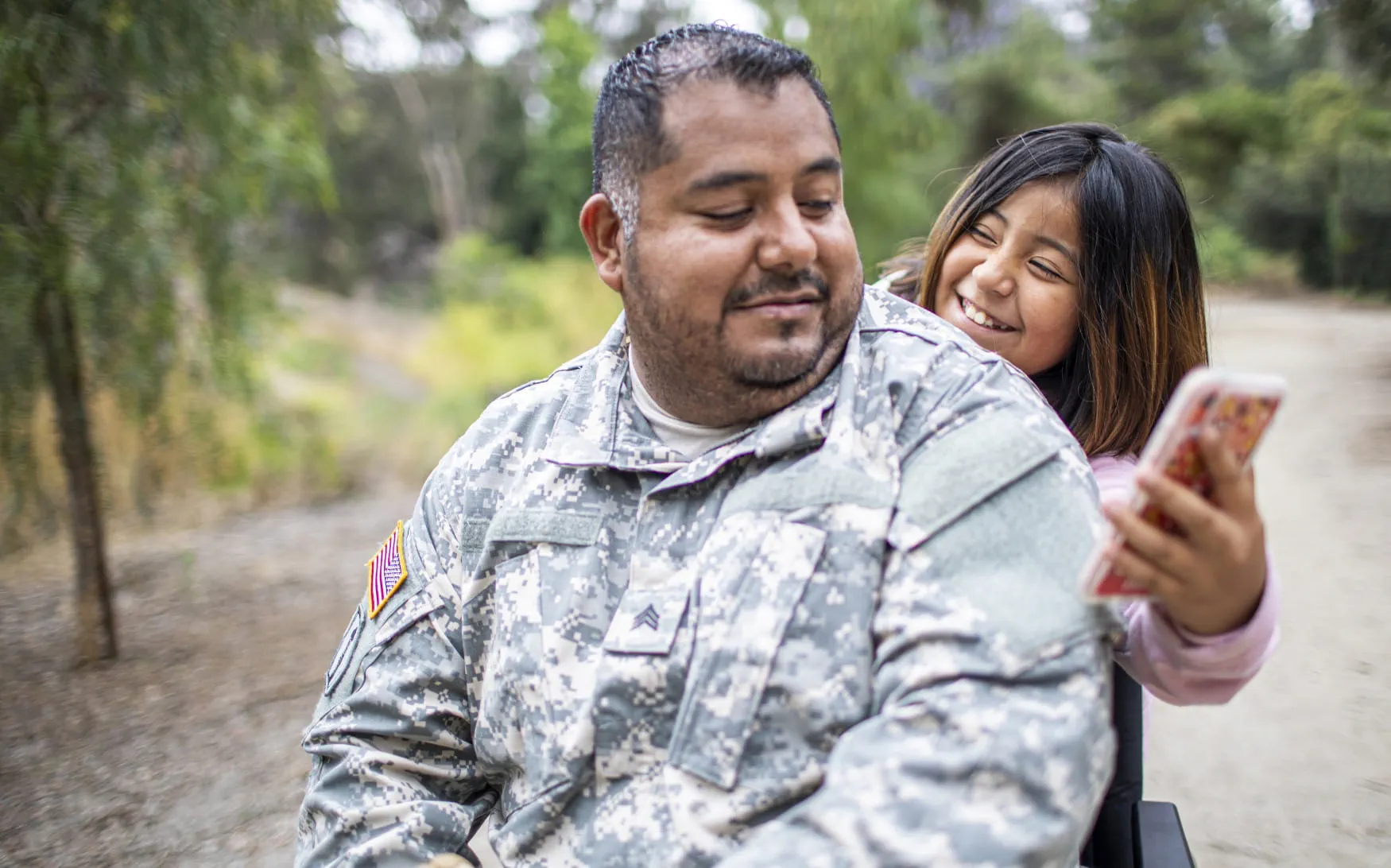 Man in a military uniform smiling with a young girl, who is showing him something on her phone.