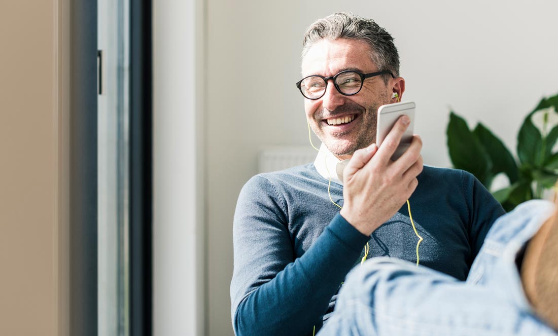 Person smiling with earbuds in, holding a phone while looking into the distance.