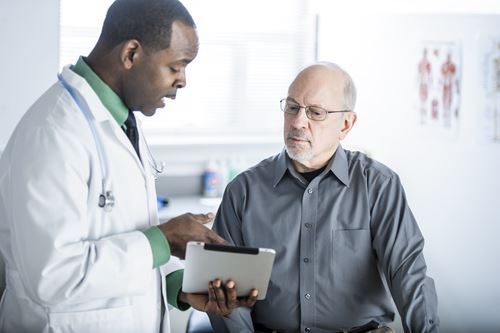 Healthcare provider reviewing information on a tablet with an older male patient in a medical office setting.