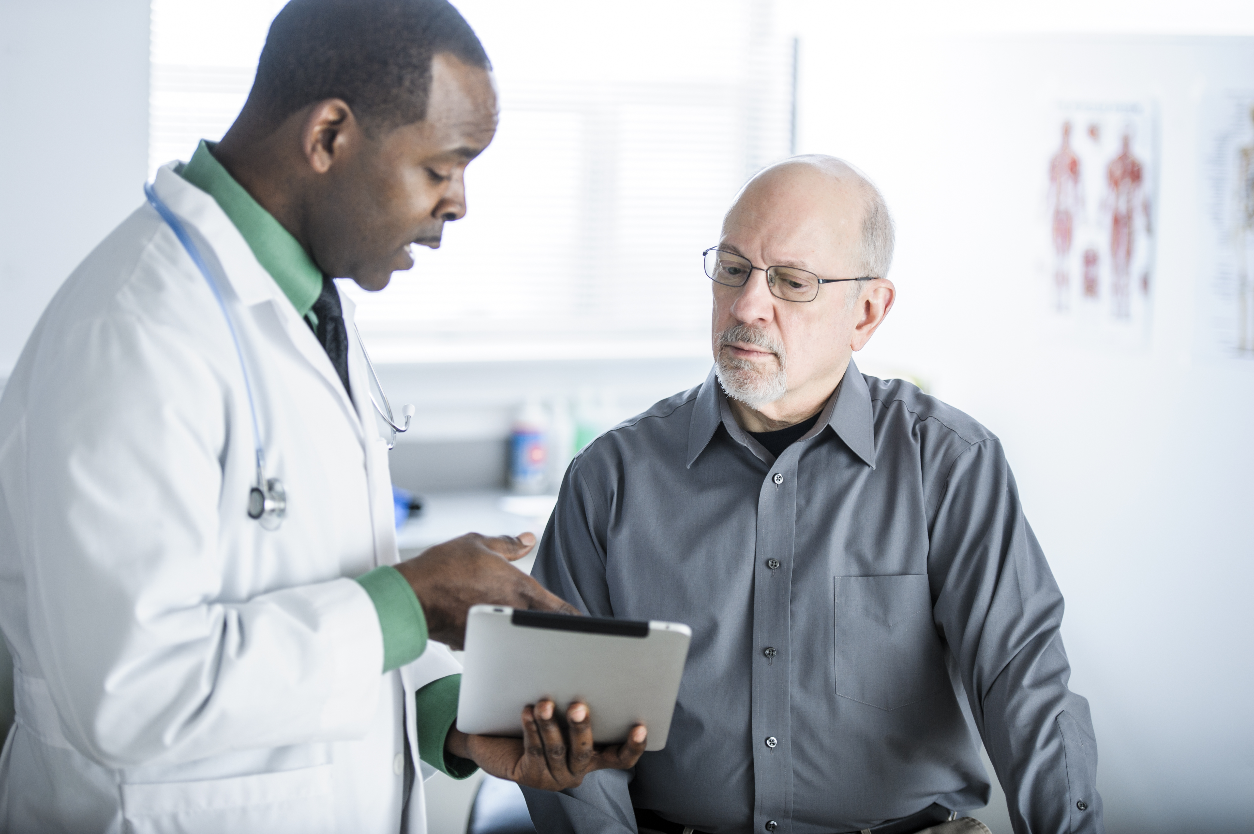 Healthcare provider reviewing information on a tablet with an older male patient in a medical office setting