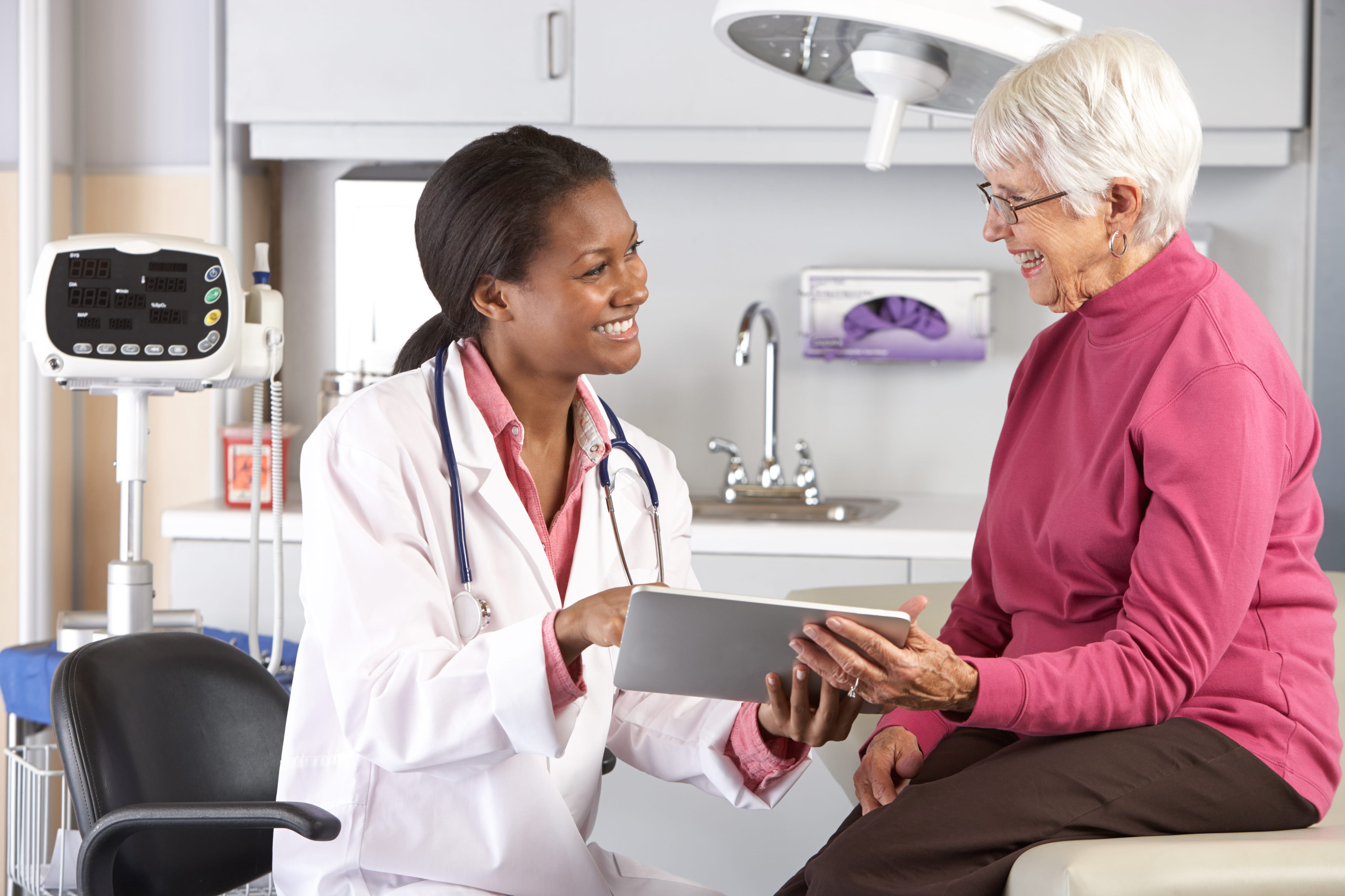 Healthcare provider reviewing information on a tablet with an older female patient during an office visit.