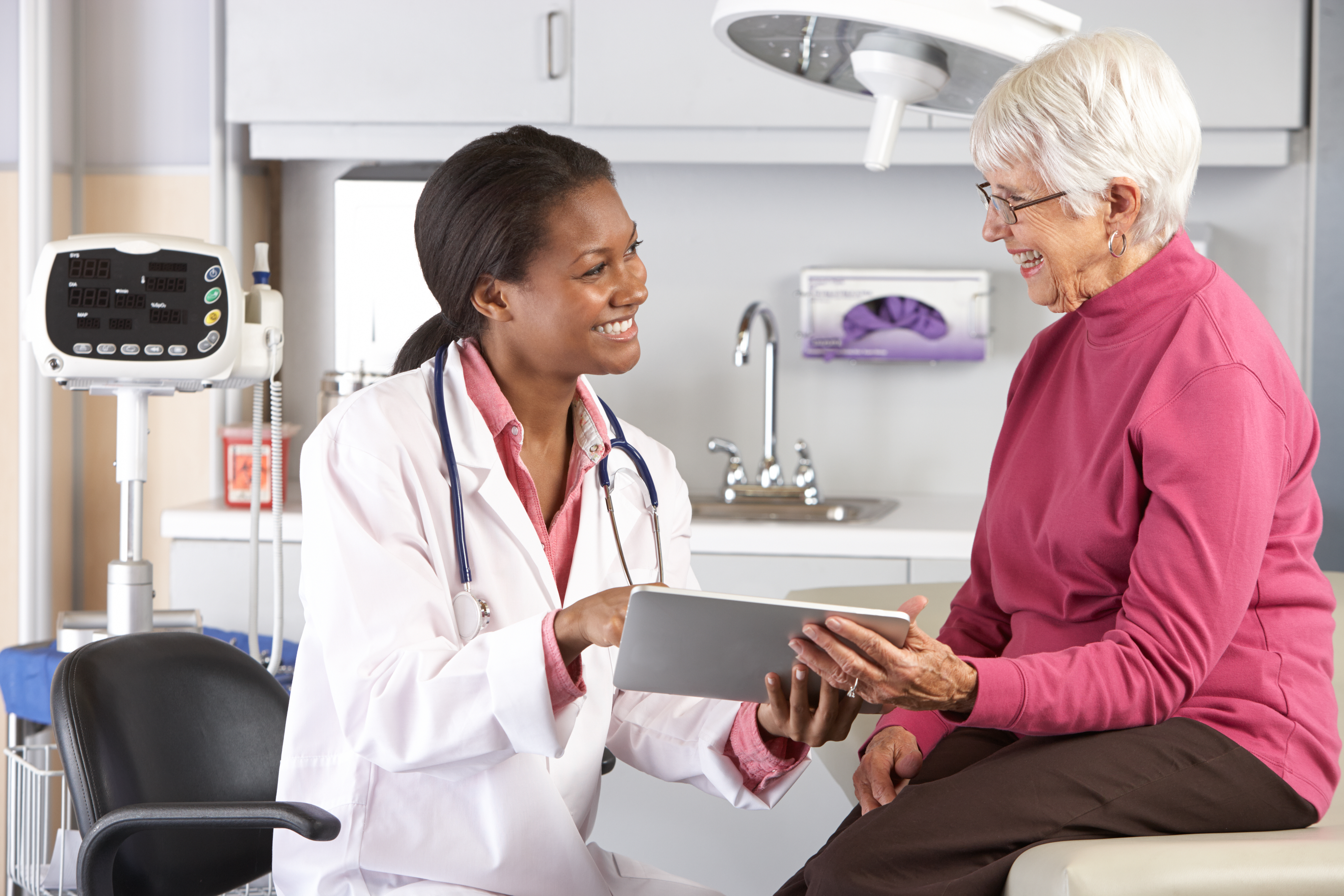 Healthcare provider reviewing information on a tablet with an older female patient during an office visit