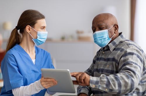 Masked healthcare provider reviewing information on a tablet with a masked patient during an office visit.